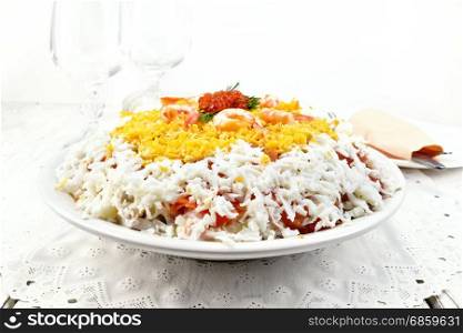 Layered salad of salmon, squid, shrimp, avocado, rice and eggs in a plate, napkin on the background light wooden boards