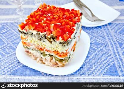 Layered salad with chicken, egg, mushrooms and cucumber, carrots and pepper, mayonnaise in a dish on the background of the tablecloth