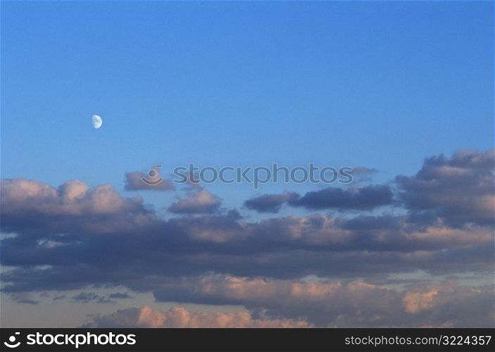 Layers Of Clouds With The Moon In A Clear Blue Sky