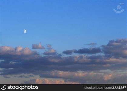 Layers Of Clouds With The Moon In A Clear Blue Sky