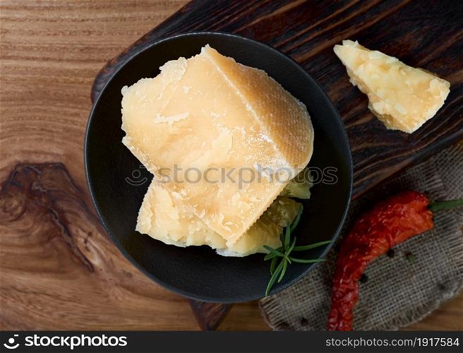 Layout of hard cheese on a dark background with spices. Pieces of parmesan cheese in a black plate.