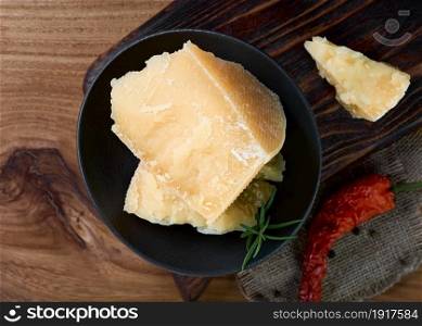 Layout of hard cheese on a dark background with spices. Pieces of parmesan cheese in a black plate.