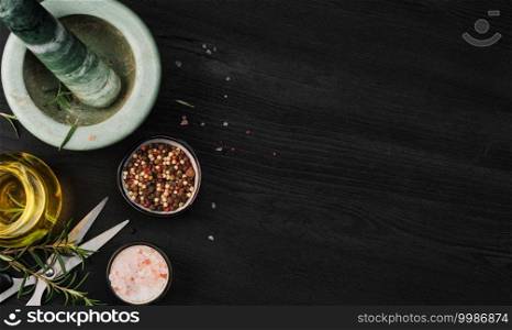 Layout of products for cooking seasoning in a marble mortar. Composition with sea salt, rosemary, olive oil and various types of pepper on a dark wooden background, top view with copy space