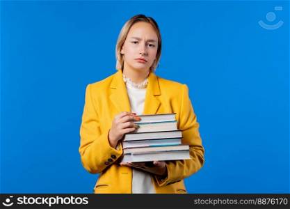 Lazy woman or student is dissatisfied with amount of books homework on blue background. Girl in displeasure, she is annoyed, discouraged frustrated by studies. High quality photo. Lazy student woman is dissatisfied with amount of books homework on blue