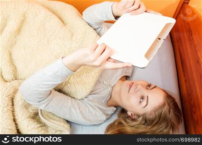 Lazy young woman using computer tablet browsing internet. Girl laying in bed under blanket and holding ebook. Technology leisure.. Young woman girl with tablet browsing internet.