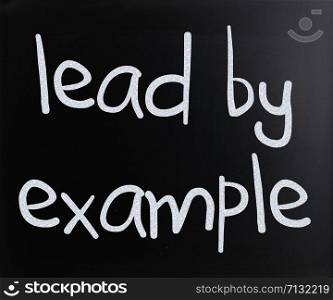 ""Lead by example" handwritten with white chalk on a blackboard"