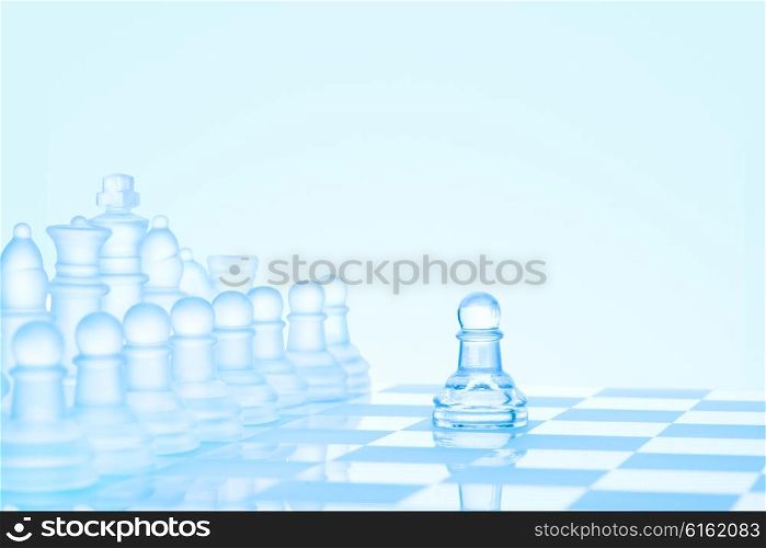 Leadership and bravery concept; an icy frosted single pawn staying against a full set of chess pieces on chessboard.