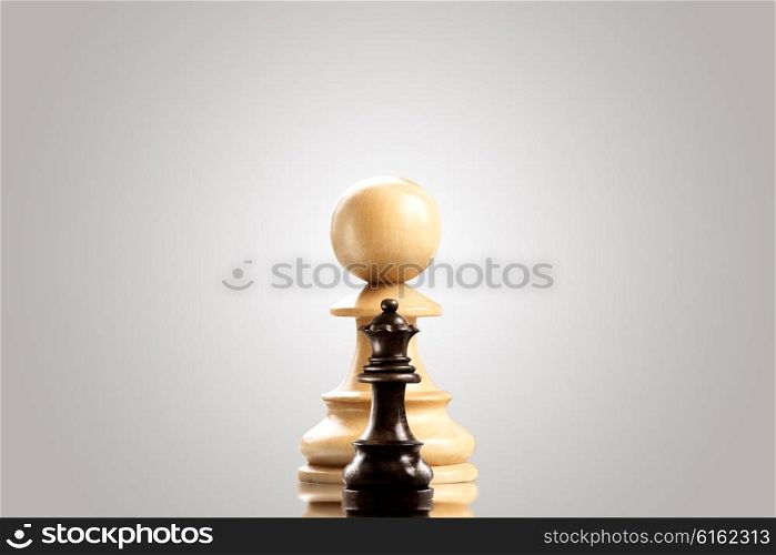 Leadership and bravery concept; huge white wooden pawn staying against a small black queen.