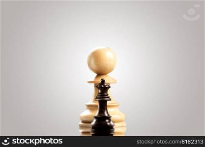 Leadership and bravery concept; huge white wooden pawn staying against a small black queen.