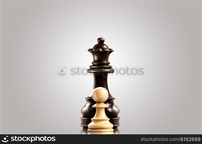 Leadership and bravery concept; white wooden single pawn staying against a black queen.