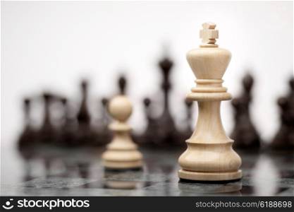 Leadership and bravery concept; white wooden single pawn staying against a white king on chessboard.