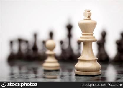 Leadership and bravery concept; white wooden single pawn staying against a white king on chessboard.
