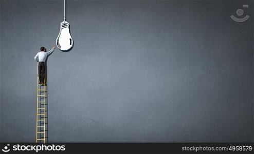Leadership concept. Back view of businessman standing on ladder and reaching light bulb