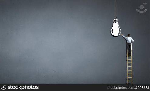 Leadership concept. Back view of businessman standing on ladder and reaching light bulb