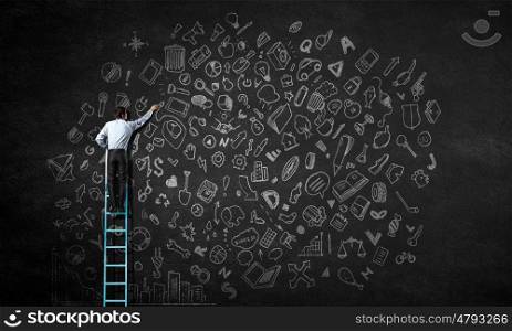 Leadership concept. Rear view of businessman standing on ladder and writing business concepts on wall
