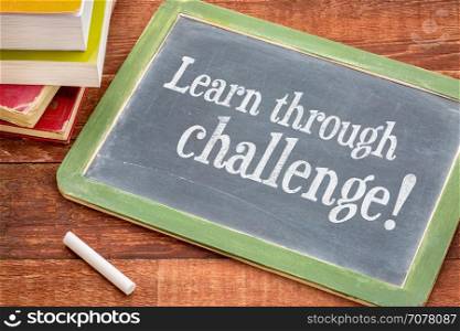 Learn through challenge motivational concept - white chalk text on a slate blackboard with a stack of books against rustic wooden table
