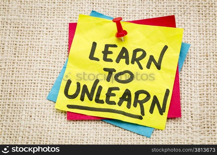 learn to unlearn - advice or motivation words on a sticky note against burlap canvas