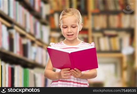 learning, education and school concept - smiling little girl reading book over library shelves background. smiling little girl reading book at library