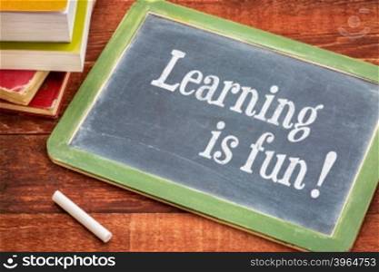 Learning is fun - inspirational text on a slate blackboard with a white chalk and a stack of books against rustic wooden table