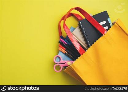 Learning supplies with notebooks, coloured pens and scissors in yellow bag on yellow background with copy space for education and back to school concept
