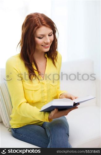 leasure and home concept - smiling teenage girl reading book and sitting on couch at home