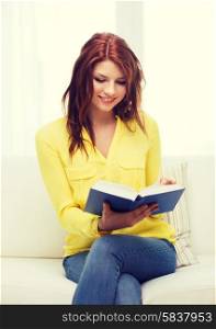 leasure and home concept - smiling teenage girl reading book and sitting on couch at home
