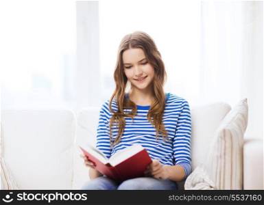 leasure and home concept - smiling teenage girl woman reading book and sitting on couch at home