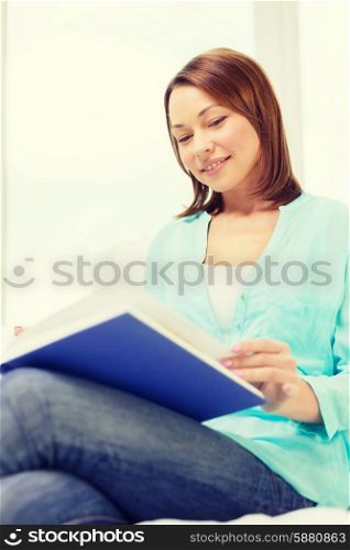 leasure and home concept - smiling woman reading book and sitting on couch at home