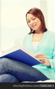 leasure and home concept - smiling woman reading book and sitting on couch at home