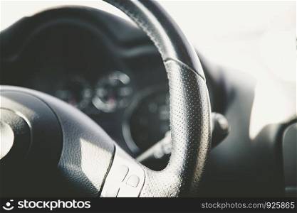 Leather-black steering wheel of a modern car, blurry dashboard