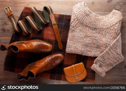 Leather boots with sweater and female clothes at wooden table. Travel concept of retro clothing