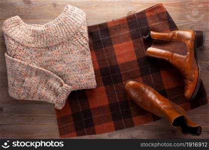 Leather boots with sweater and female skirt at wooden table. Modern concept of retro clothing