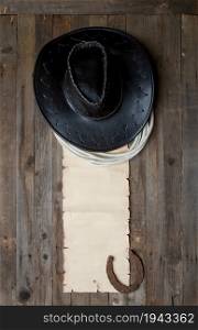 leather classic cowboy hat with lasso and horseshoe on rough wooden table and blank paper with place for text
