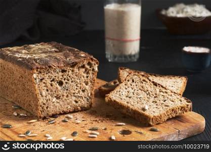 Leavened bread, whole grain rye bread with pumpkin and sunflower seeds. Leaven starter on table. Authentic sourdough homemade bread-organic bio product. Handcrafted product, slices of bread on board