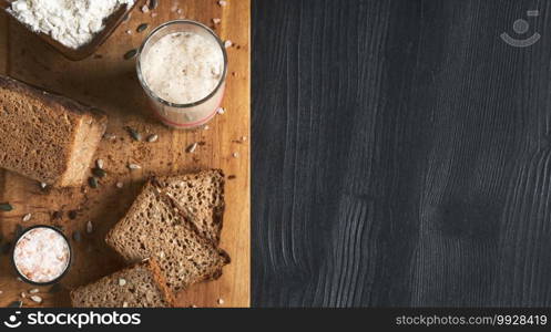 Leavened bread, whole grain rye bread with pumpkin and sunflower seeds. Leaven starter on table. Authentic sourdough bread, organic bio product. Top view with copy space, slices of bread board