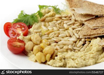 Lebanese hummus with pine-nuts on a plate with some flat bread, sliced cherry tomatoes and a garnish of young salad leaves, topped off with a drizzle of olive oil