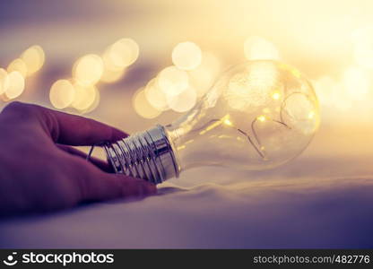 LED light bulb is lying in the bed, hands touching. Symbol for ideas and innovation. Spot lights in the blurry background.