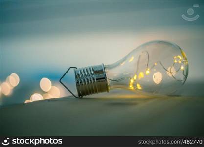LED light bulb is lying on a wooden table. Symbol for ideas and innovation. Spot lights in the blurry background.