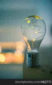 LED light bulb is lying on a wooden table. Symbol for ideas and innovation. Spot lights in the blurry background.