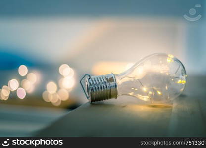 LED light bulb is lying on a wooden table. Symbol for ideas and innovation. Spot lights in the blurry background.