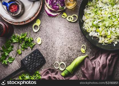 Leeks meal eating and cooking . Pan with sliced leeks on kitchen table background with tools and ingredients, top view, frame
