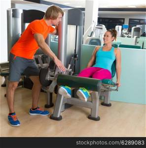 Leg extension exercise woman at gym indoor workout with personal trainer blond man