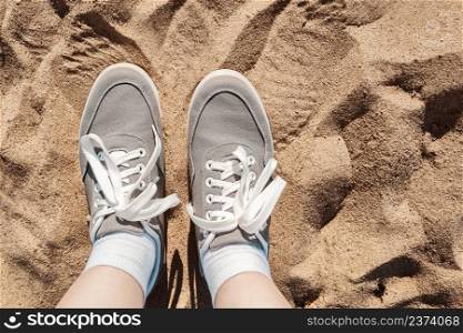 Legs in gray sneakers on the beach sand. Summer vacation concept by the sea. Lifestyle travel. Pov view. Copy space.. Legs in gray sneakers on beach sand. Summer vacation concept by the sea. Lifestyle travel. Pov view. Copy space.