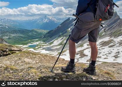 legs of a hiker wearing short and hiking shoes standing at the top of mountain with beautiful alpine landscape