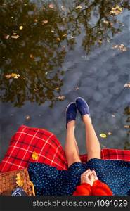 Legs of a young girl near the lake on a plaid in a red cage. Beautiful reflection in the water. View from above. Legs of a young girl near the lake on a plaid in a red cage. Beautiful reflection in the water. View from above.