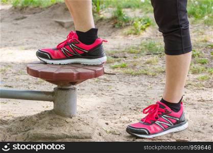 Legs of elderly senior woman in sports shoes exercising on outdoor gym in sunny park, trainer machine, healthy, sporty lifestyles and slimming concept. Legs of elderly senior woman on outdoor gym, healthy lifestyle concept