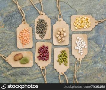 legume abstract (fava bean, red lentils, adzuki bean, soy, mung bean,navy bean, yellow pea, French lentils) - top view of paper price tags against slate stone