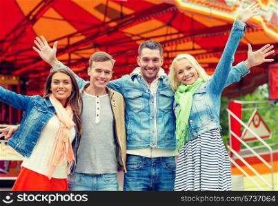 leisure, amusement park and friendship concept - group of smiling friends waving hands with carousel on the back