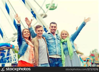 leisure, amusement park and friendship concept - group of smiling friends waving hands with ferris wheel on the back
