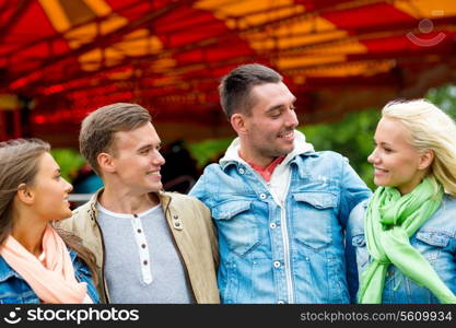 leisure, amusement park and friendship concept - group of smiling friends with carousel on the back